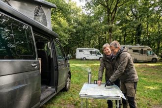 Couple souriant pointant une carte devant leur van moderne