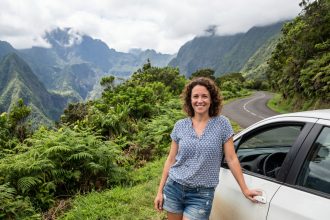 Femme souriante devant une voiture à Réunion avec paysage volcanique