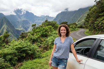 Femme souriante devant une voiture à Réunion avec paysage volcanique