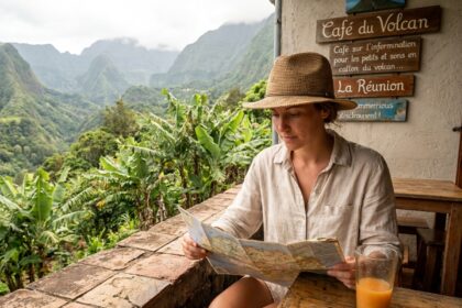 Voyageuse consultant une carte touristique sur une terrasse à La Réunion avec vue sur un paysage volcanique tropical